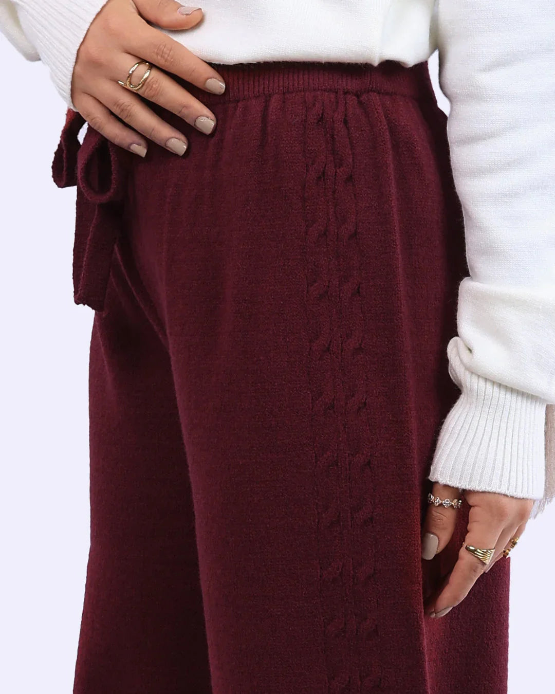 Close-up of burgundy knit pants with cable detail and tie waist, styled with a white sweater