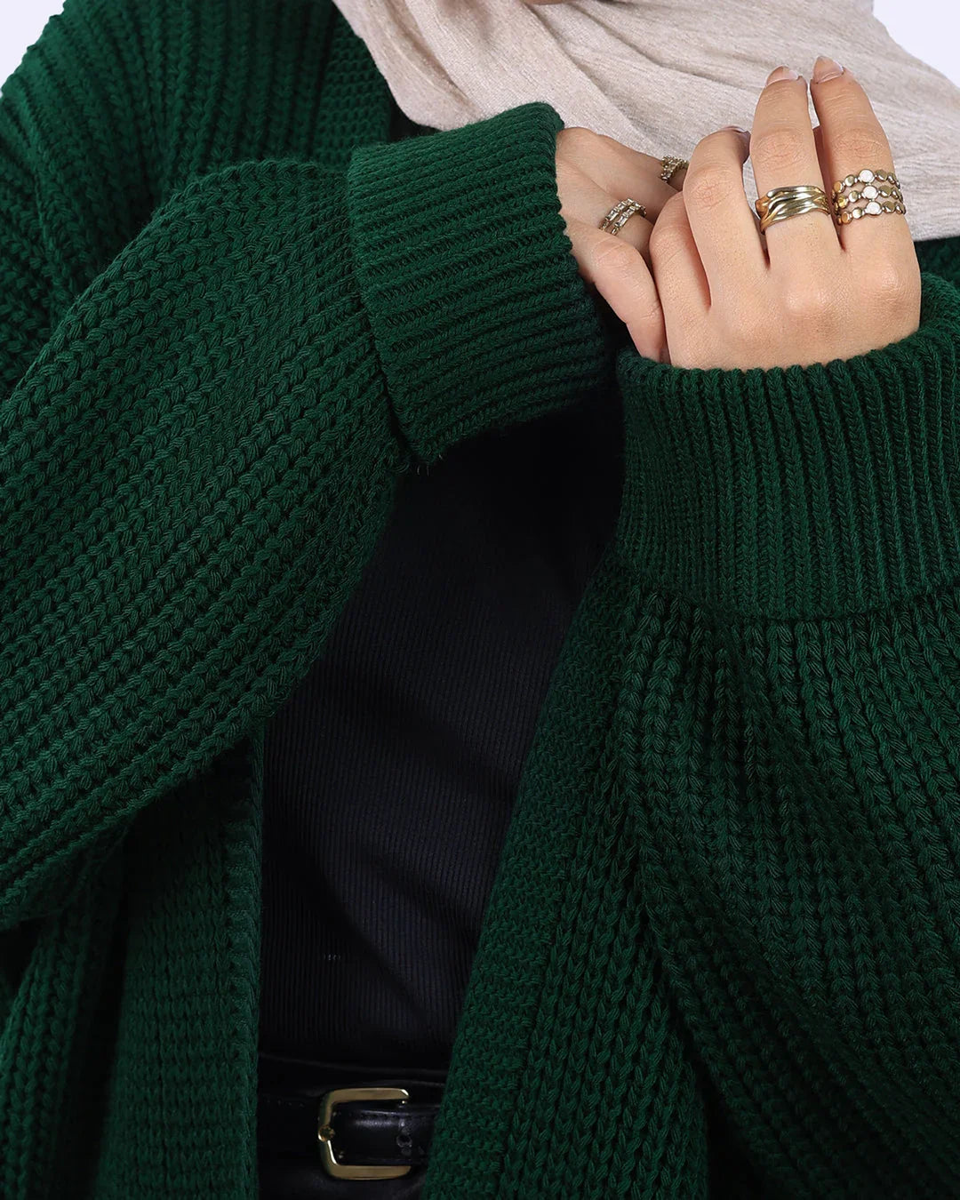 Woman wearing chunky green knit cardigan, black top, gold rings, and beige scarf from WIND Shopping