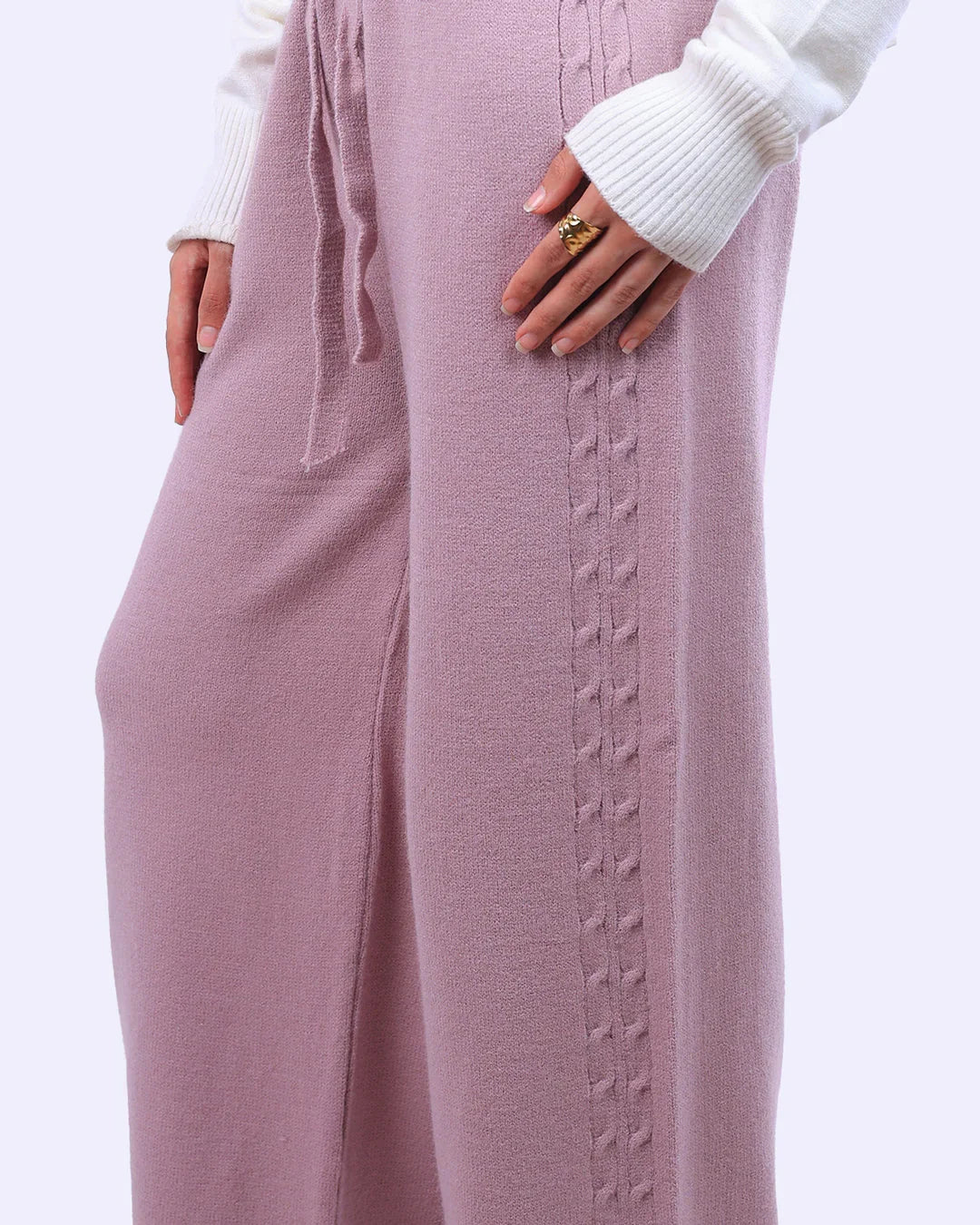 Close-up of pastel pink knit pants with braided detail, styled with a white ribbed sweater from WIND Shopping.