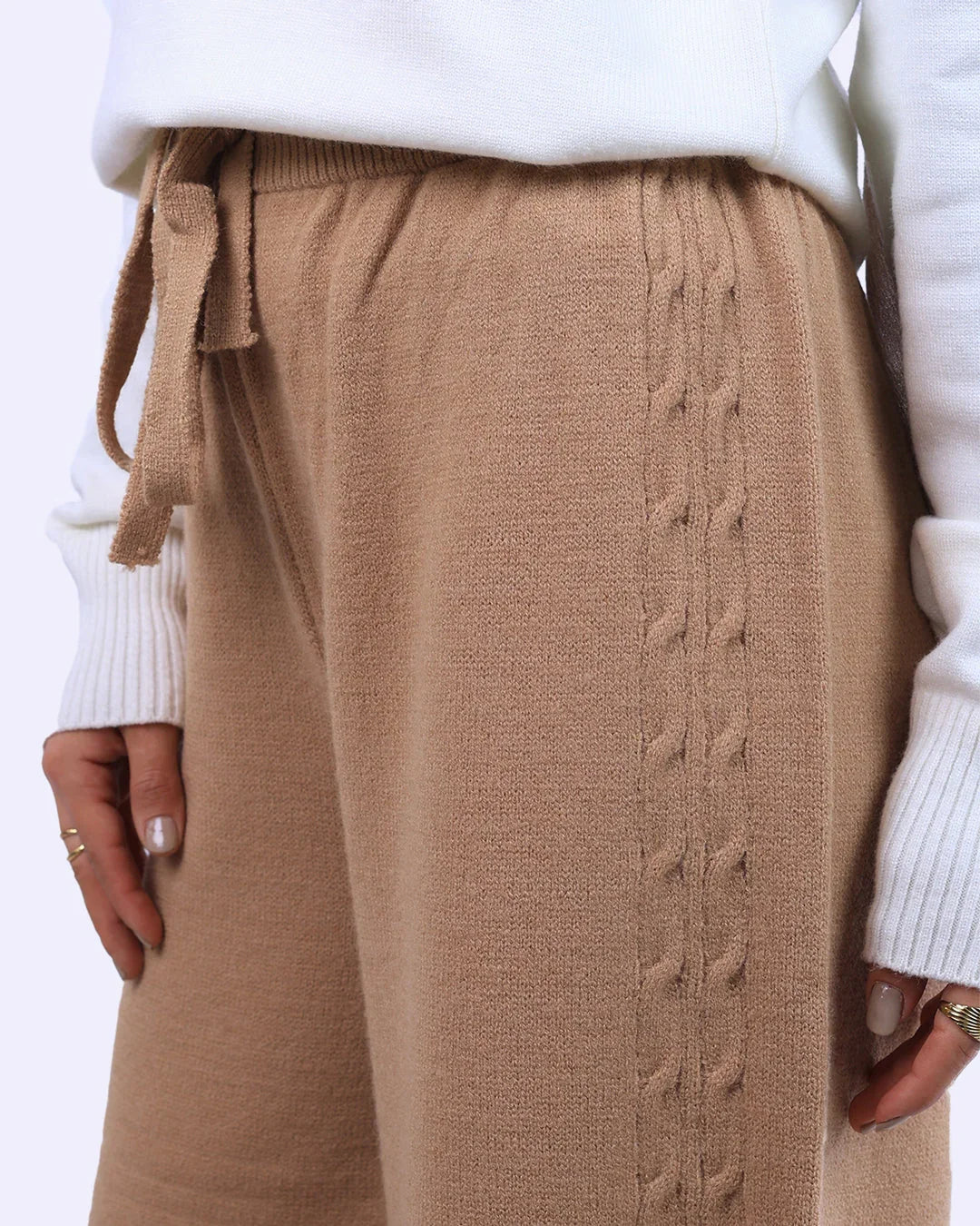 Beige knit pants with side cable detail and tie waist, styled with white sweater from WIND Shopping.