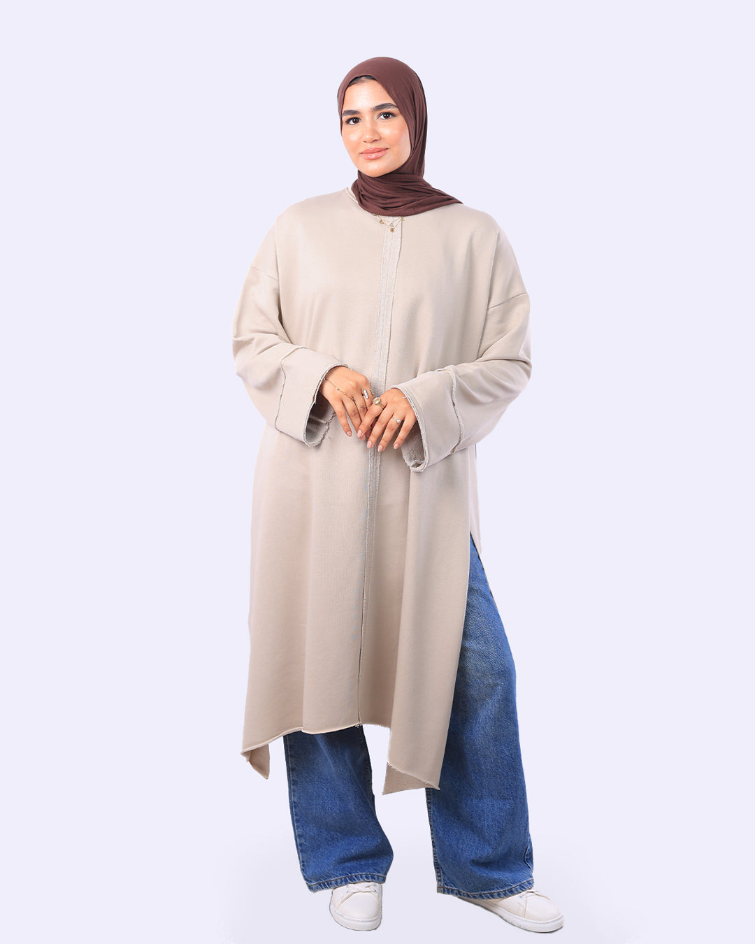 Woman wearing a beige long-sleeve top and blue jeans on a white background