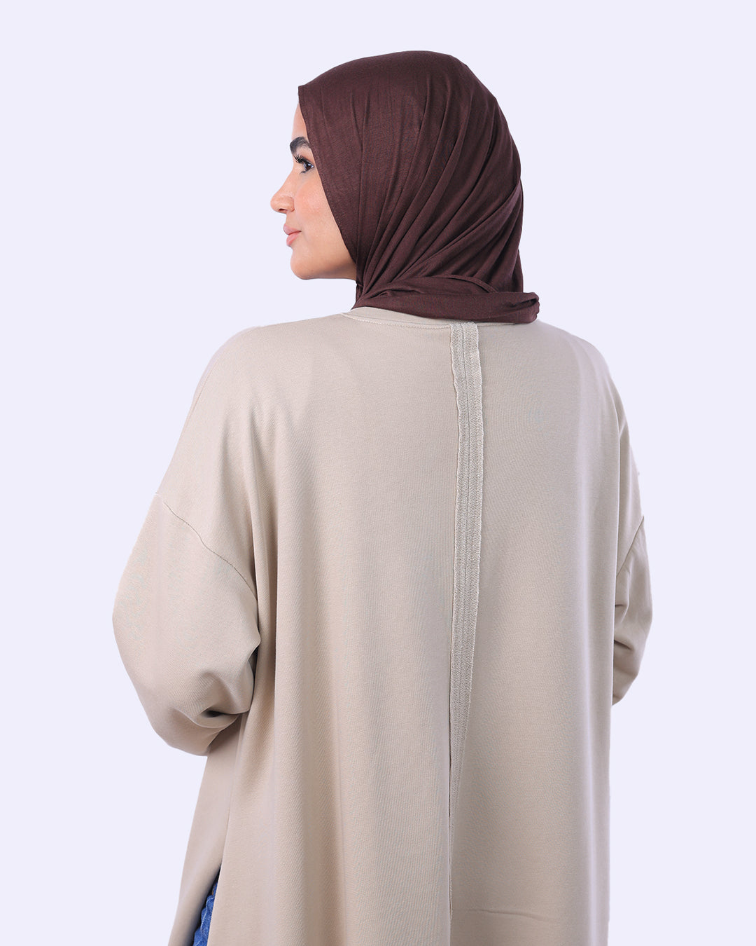 Woman wearing a beige abaya and brown hijab on a white background