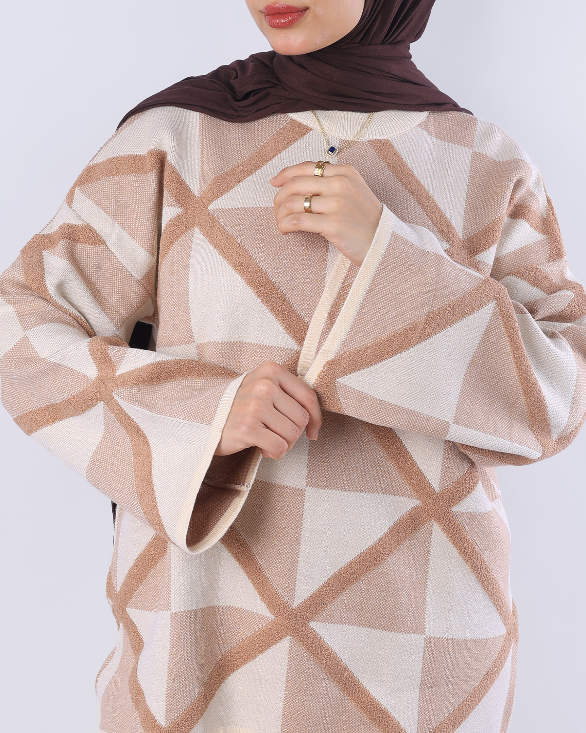 Person wearing a patterned beige and white garment with a brown hijab on a white background