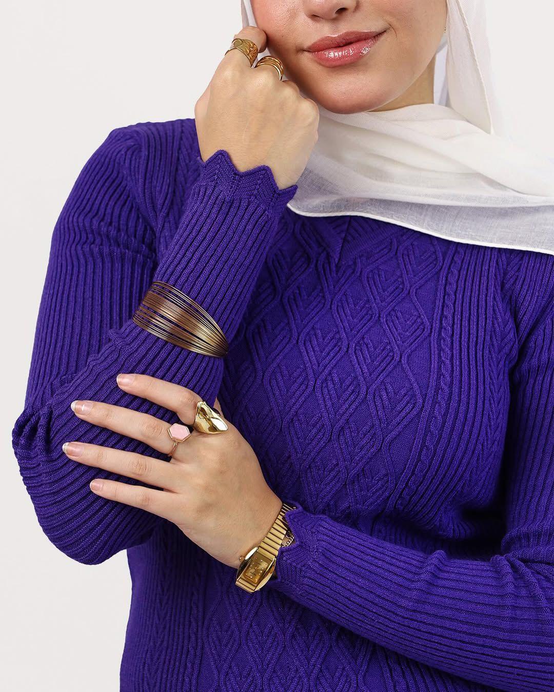 Woman in a purple sweater and white scarf modeling gold jewelry, rings, and a watch from WIND Shopping.