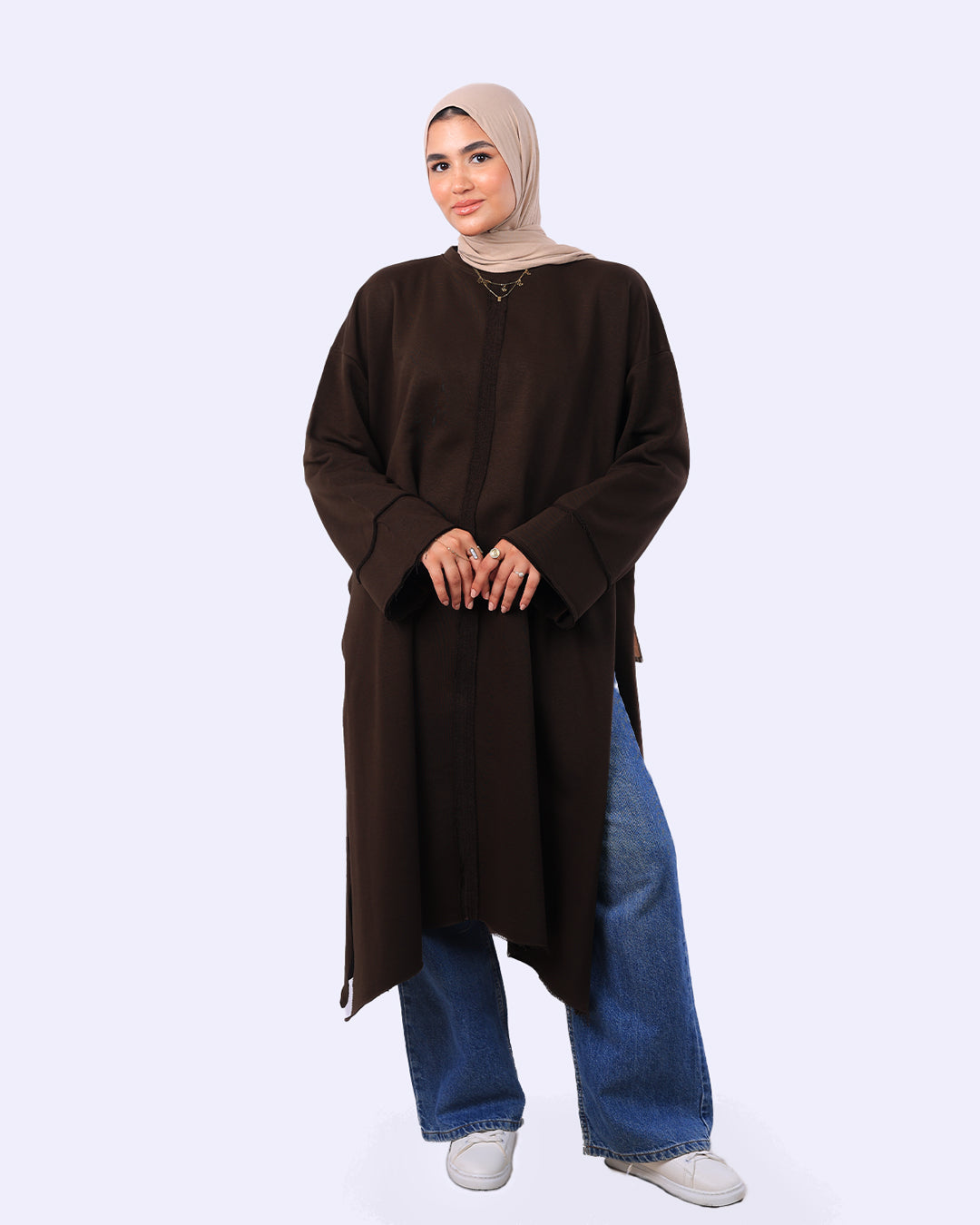 Woman wearing a brown long-sleeve top and blue jeans on a white background