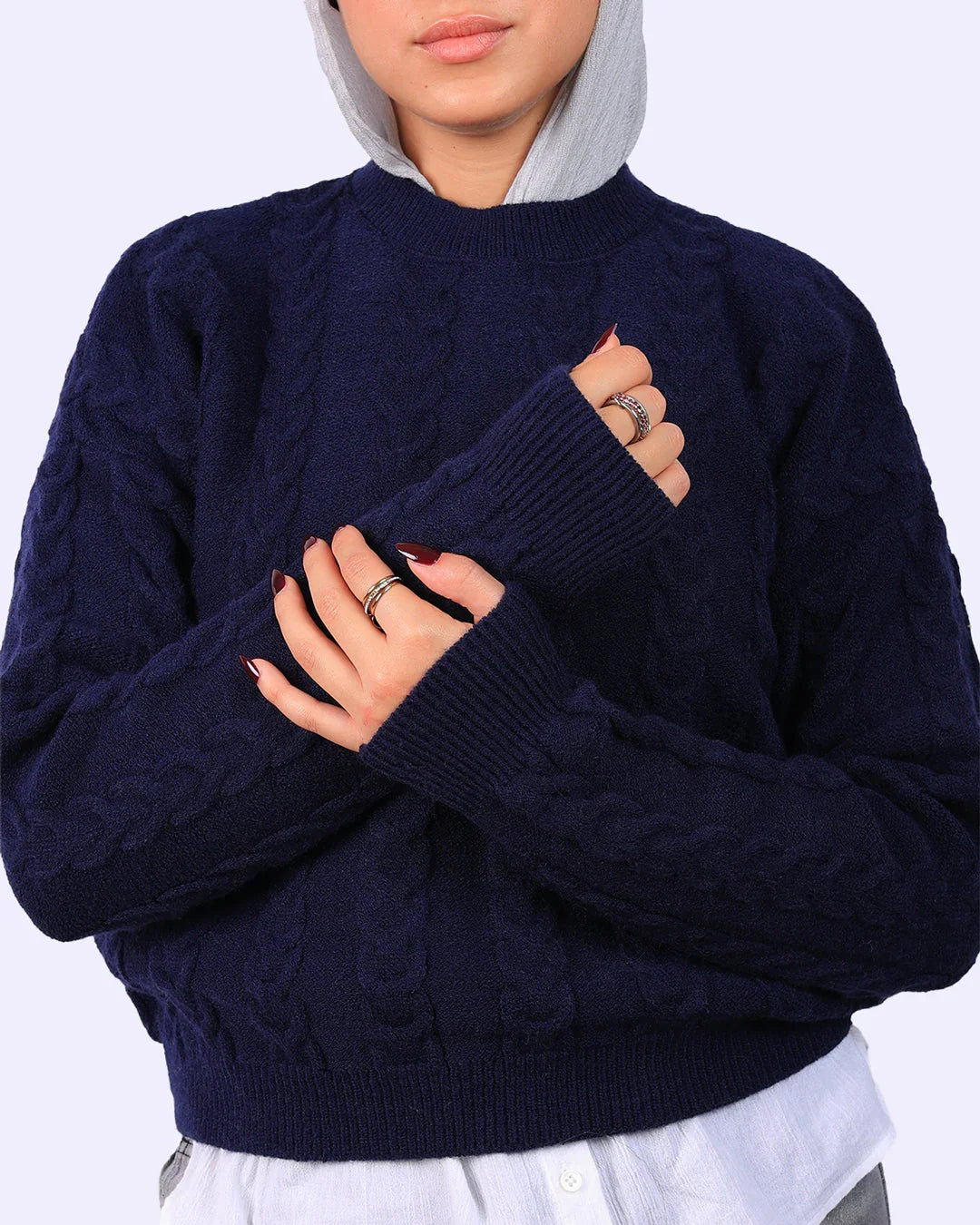 Woman in navy blue cable knit sweater from WIND Shopping, layered over white shirt, wearing rings