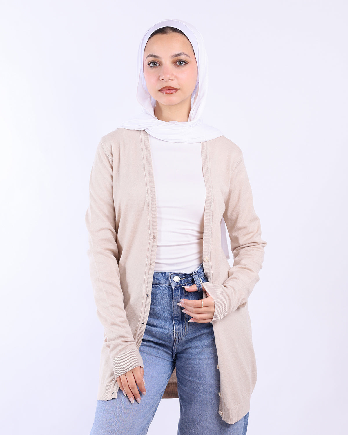 Woman wearing a beige cardigan, white top, and blue jeans on a white background- WIND Shopping
