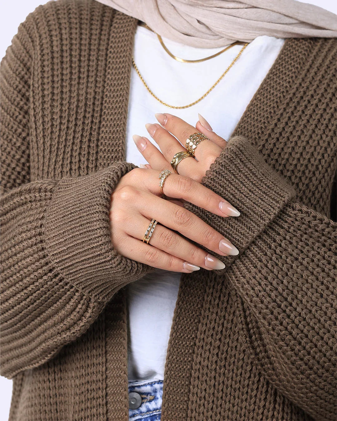 Woman wearing brown knit cardigan, gold rings and necklace, and beige hijab from WIND Shopping