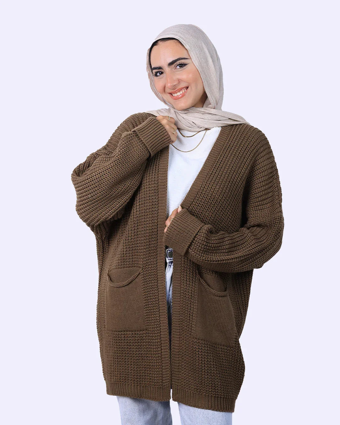 Woman in beige hijab and brown knit cardigan from WIND Shopping, smiling against light background.