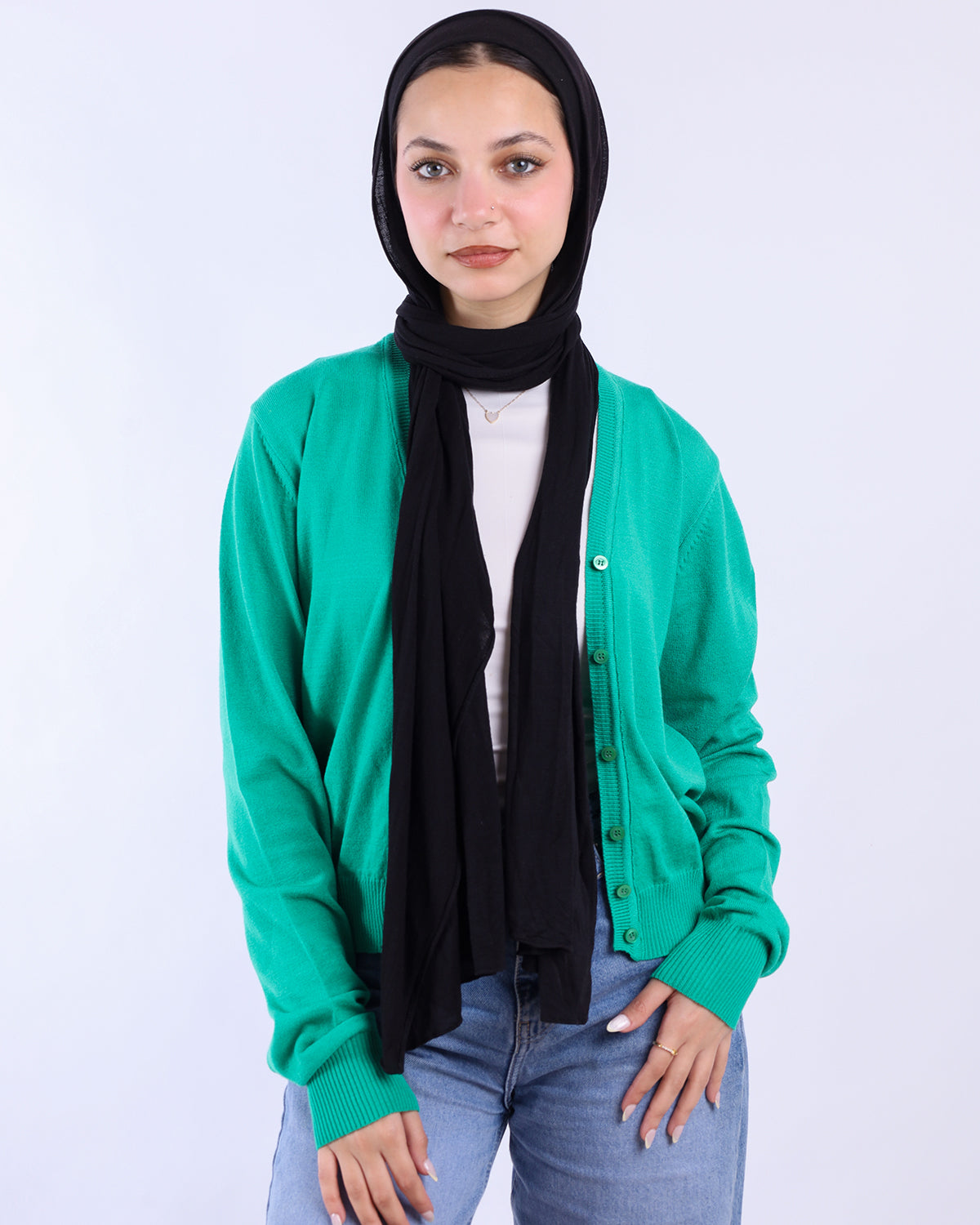 Person wearing a green cardigan, black scarf, and blue jeans on a white background- WIND Shopping