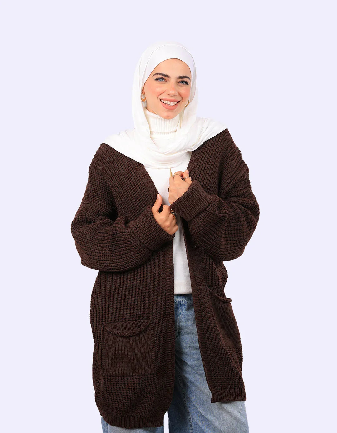 Smiling woman in white hijab and brown knit cardigan from WIND Shopping, posing against light background