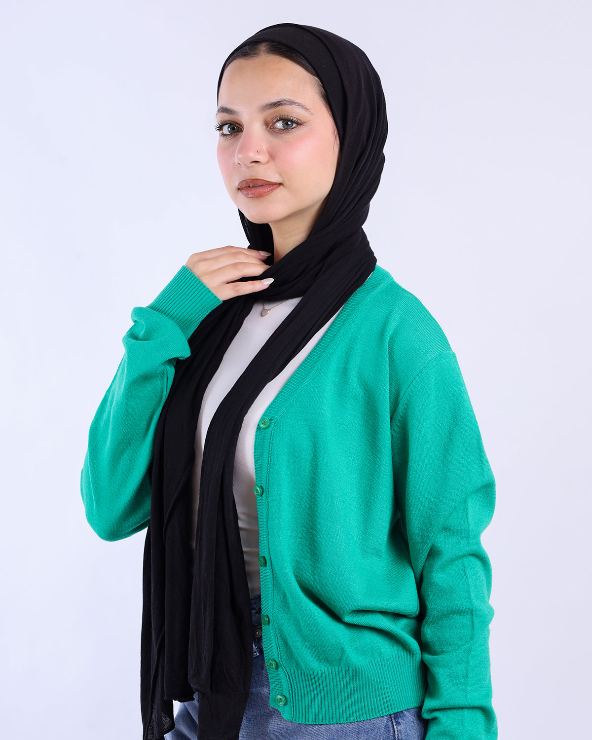 Woman wearing a green cardigan over a black hijab on a white background- WIND Shopping