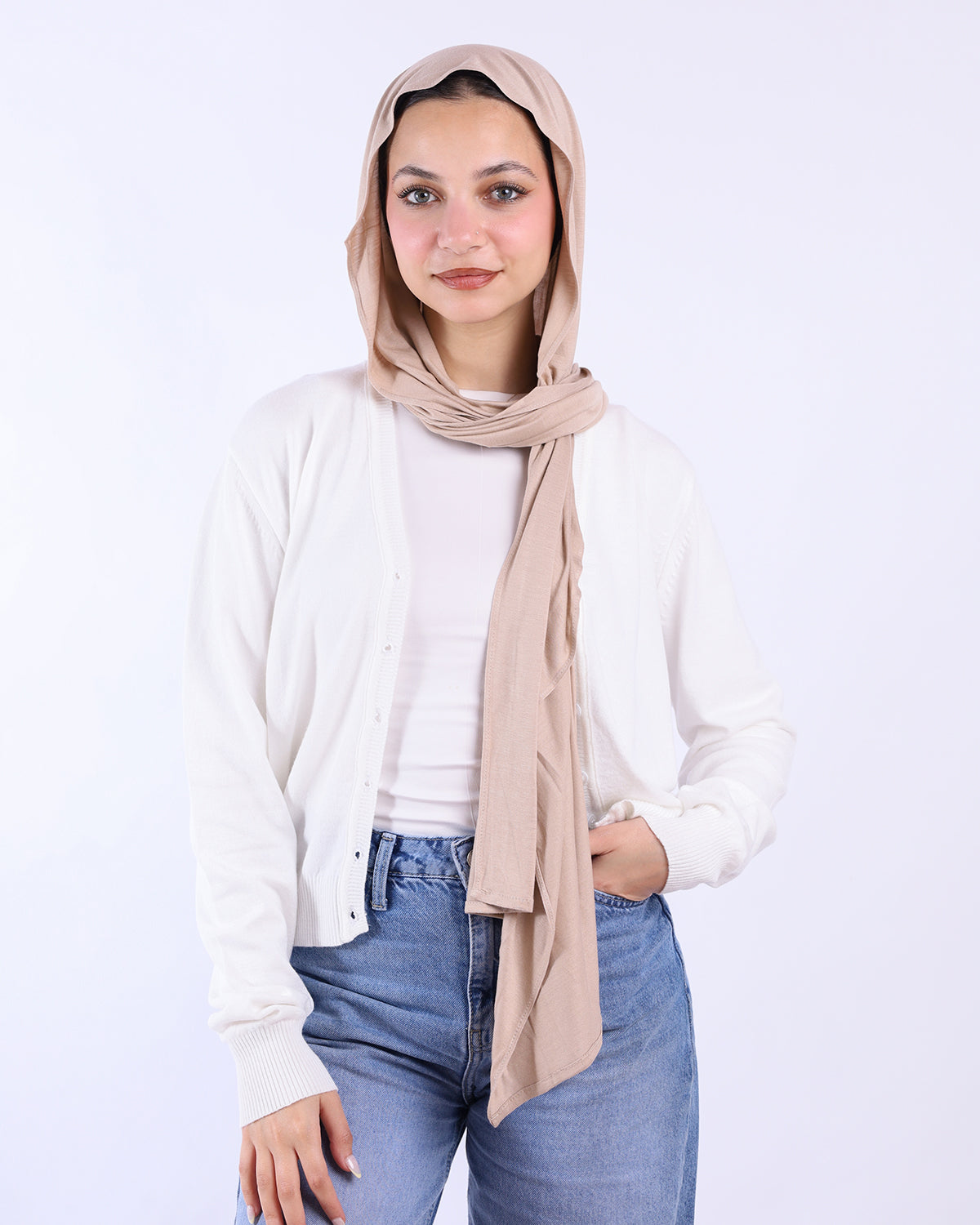 Woman wearing a beige hijab, white shirt, and blue jeans on a light gray background-WIND Shopping