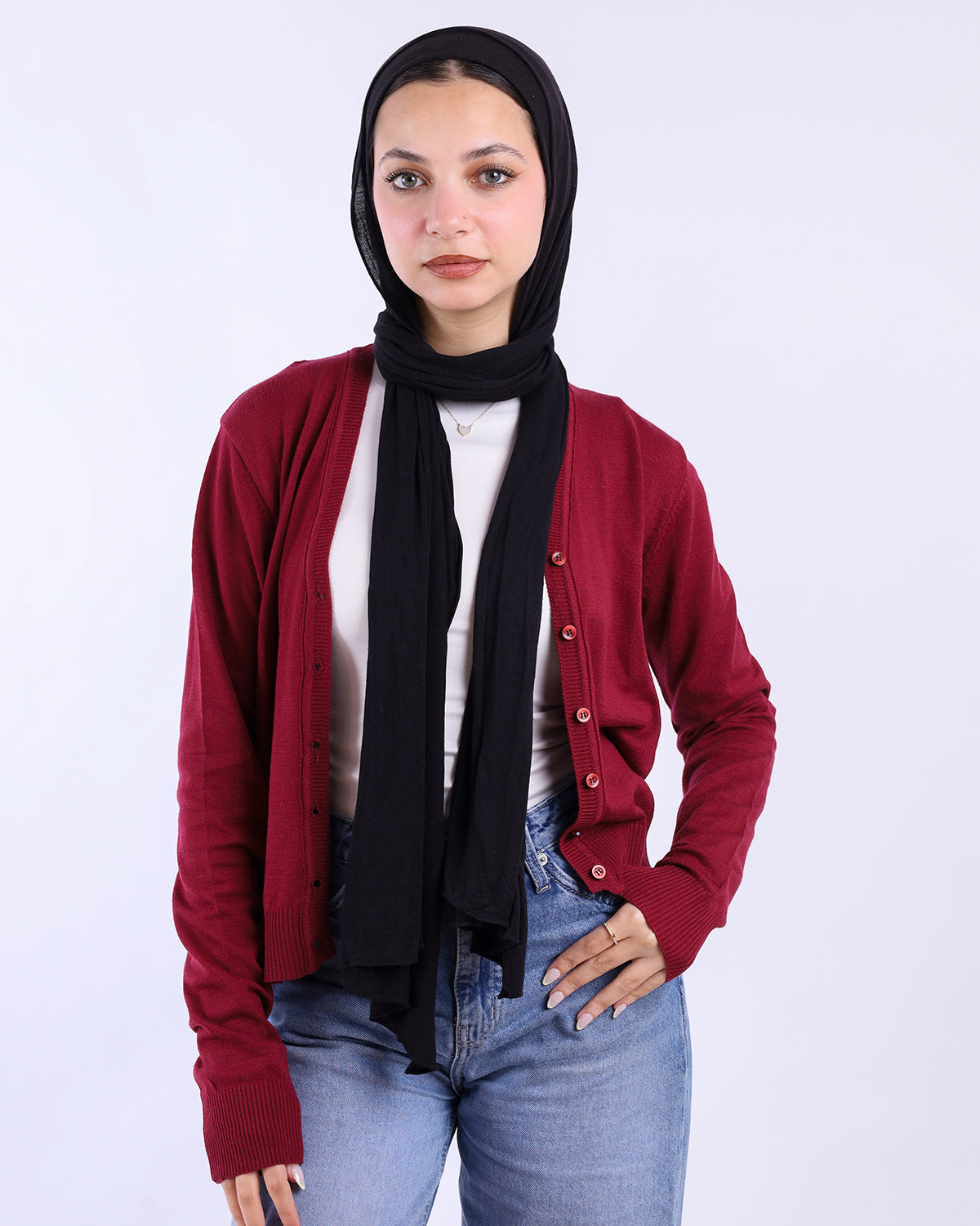Woman wearing a red cardigan, black hijab, white shirt, and blue jeans on a white background- WIND Shopping