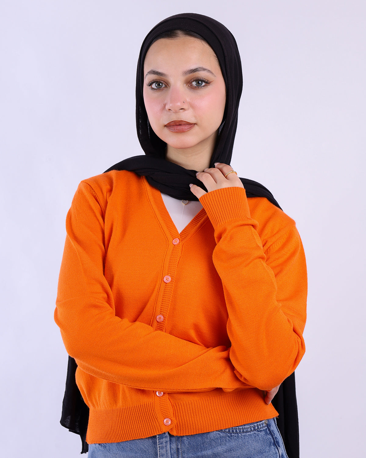 Woman wearing an orange cardigan over a black hijab on a white background- WIND Shopping