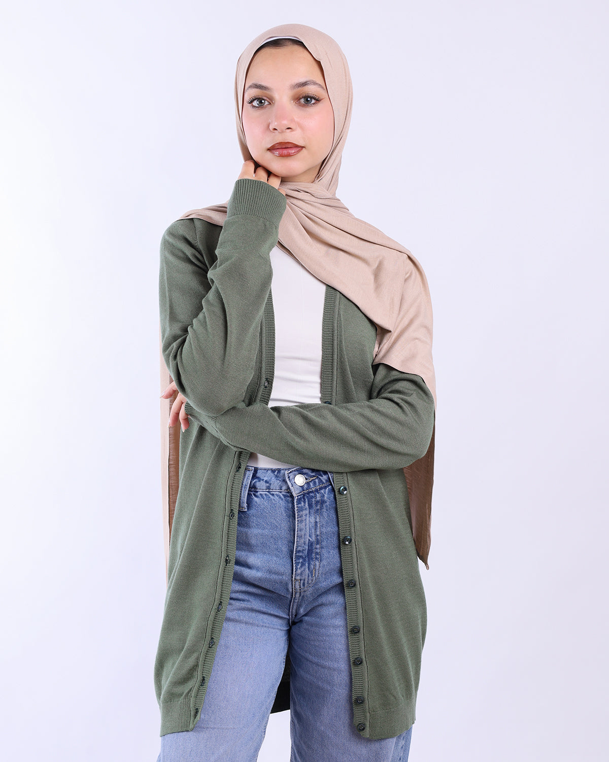 Woman wearing a green cardigan, beige hijab, white shirt, and blue jeans on a white background - WIND Shopping