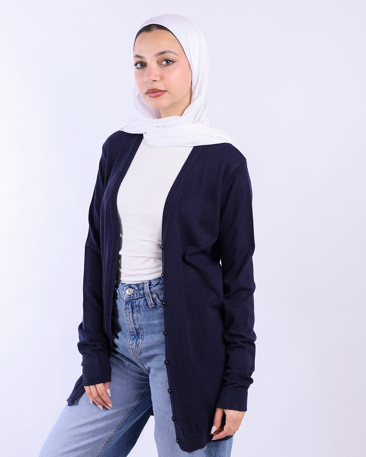 Woman wearing a navy cardigan, white top, and jeans with a white hijab on a white background- WIND Shopping